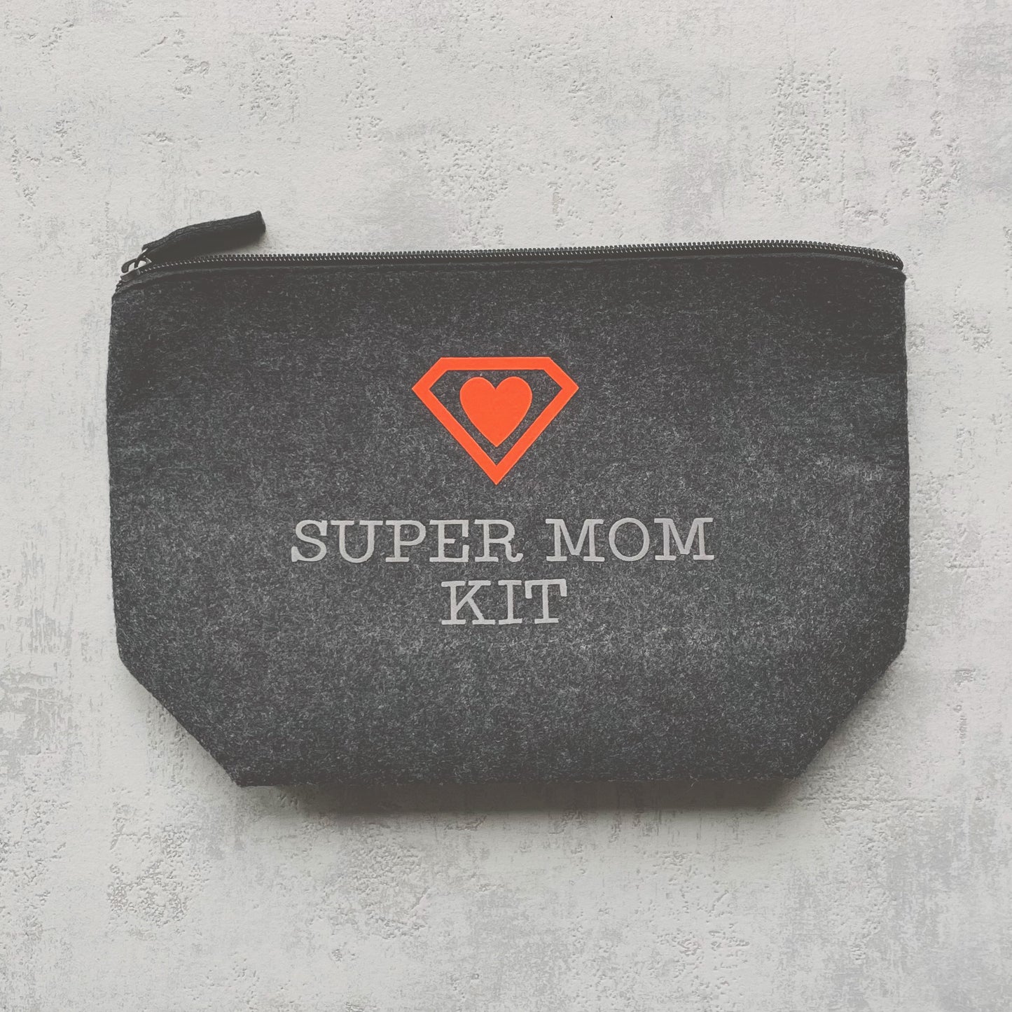 dunkelgraue Filztasche mit Superheldenaufdruck mit Herz in neonorange und dem Aufdruck "Super Mom Kit"
