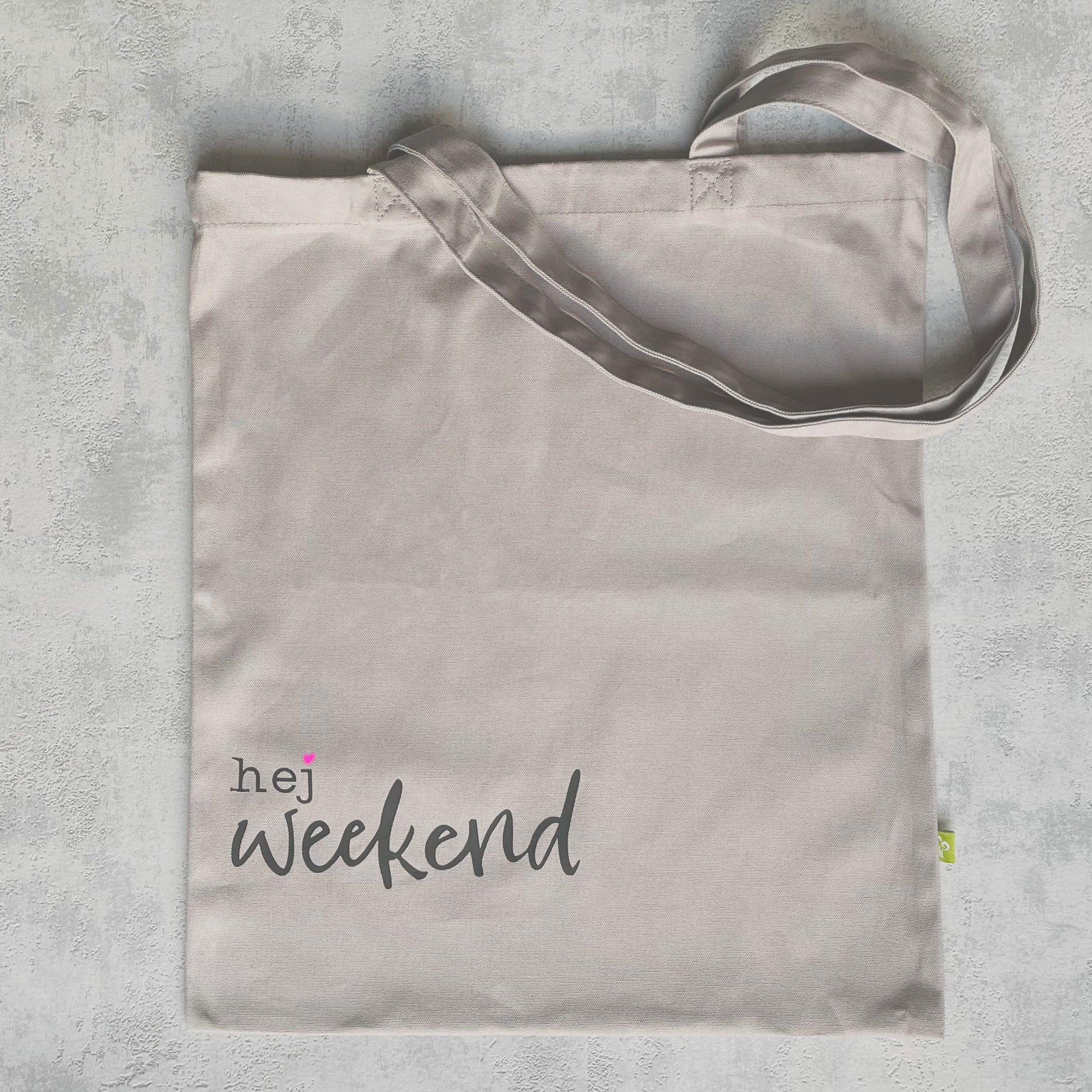 graue Einkaufstragetasche aud Canvas-Stoff (Baumwolle) mit schwarzen Schriftzu "hej weekend" mit neonpinkem Herz.